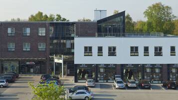 Un hôtel moderne doté d’une façade en verre, de nombreux espaces de stationnement et d’un bâtiment en briques attenant.