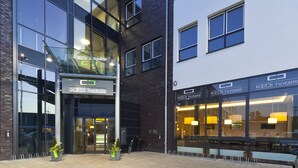 A modern hotel with a glass facade, a visible entrance, and outdoor seating. - KEDI Hotel Papenburg (Papenburg)
