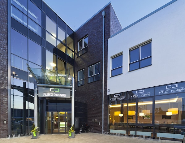 A modern hotel with a glass facade, a visible entrance, and outdoor seating.