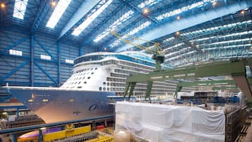 Ein großes Schiff wird in einem geräumigen Industriegebäude mit hohen Decken und sichtbaren Stahlträgern gebaut.