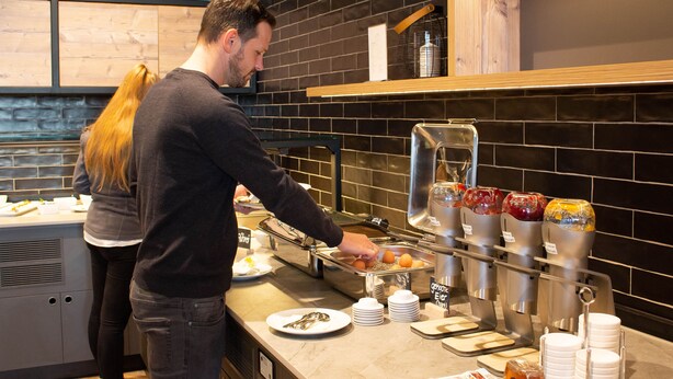 A buffet setup with various food items and a beverage dispenser. - KEDI Hotel Papenburg (Papenburg)