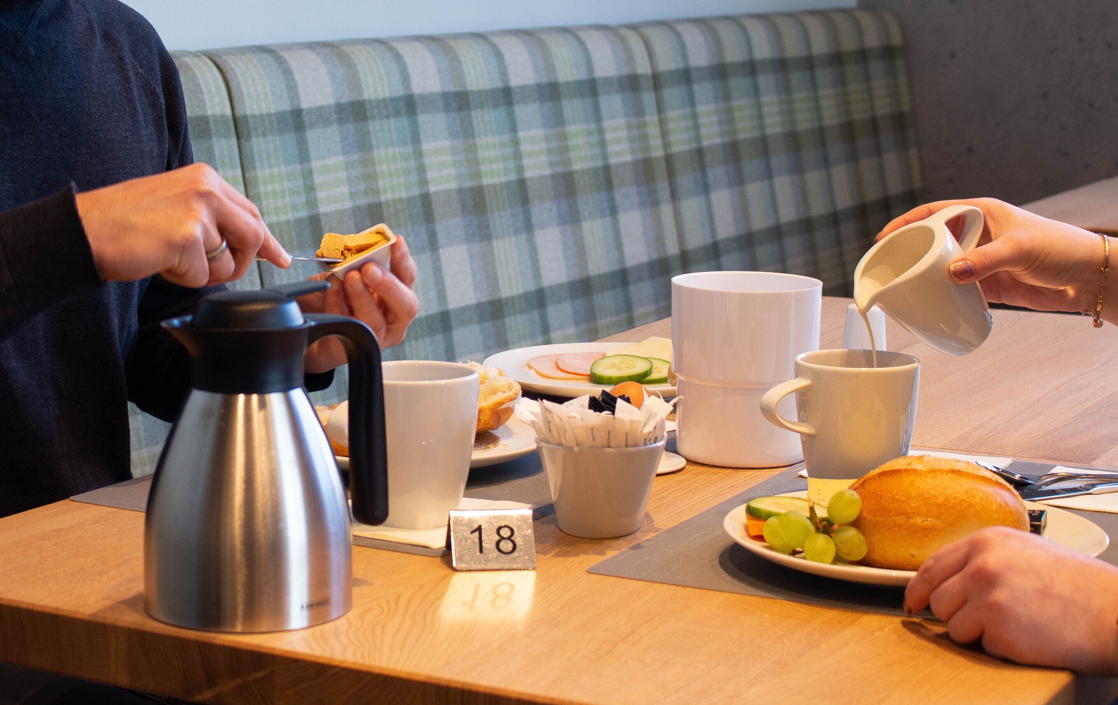 A breakfast table with a coffee pot, mugs, a plate with food, and a placemat with the number 18.