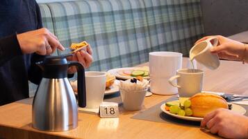 A breakfast table with a coffee pot, mugs, a plate with food, and a placemat with the number 18.