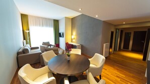 A modern hotel room with a round dining table, white chairs, a sofa, and a TV. - KEDI Hotel Papenburg (Papenburg)