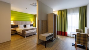 A hotel room with a bed, a desk, and a chair. There is a window with curtains. - KEDI Hotel Papenburg (Papenburg)