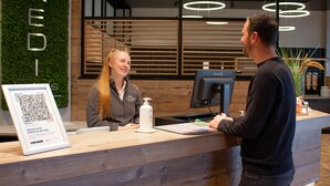 A reception desk with a QR code sign, a computer monitor, and a wooden panel wall with the word "KEDI" on it. - KEDI Hotel Papenburg (Papenburg)