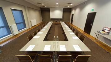 A conference room with a long table, chairs, a projector screen, and a door with an emergency exit sign.