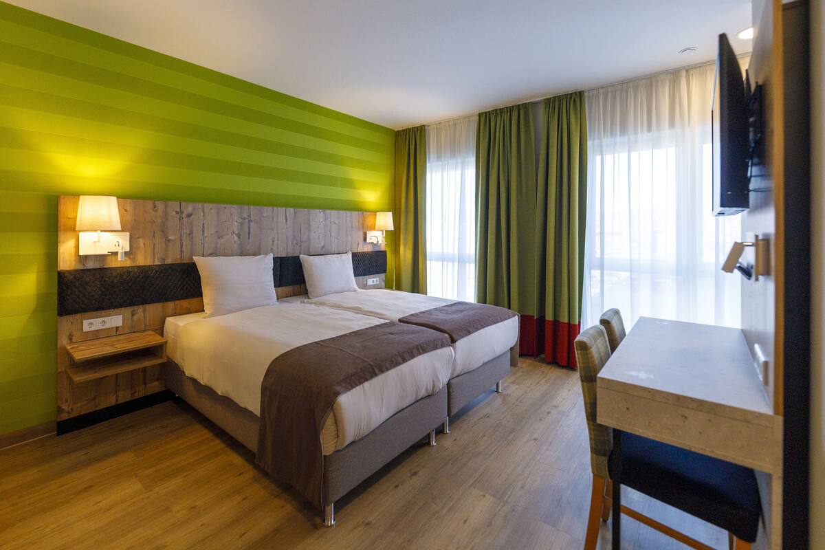 Quarto de hotel com uma cama grande, mesas de cabeceira, escrivaninha e televisão.