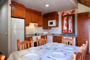 A compact kitchen with wooden cabinets, a microwave, and a dining table set for four. - Casa Pirineo, Ainsa (Ainsa)