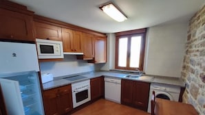 A compact kitchen with wooden cabinets, a microwave, oven, dishwasher, and a window with natural light. - Casa Pirineo, Ainsa (Ainsa)