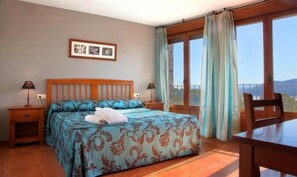 A bedroom with a bed, two bedside tables, a nightstand, a chair, and a window with curtains.