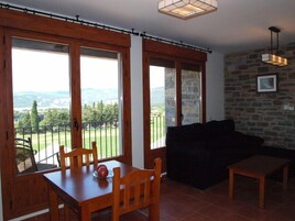 Una habitación con una mesa de comedor, sillas, un sofá, una mesita y vistas a un paisaje verde a través de amplias ventanas.