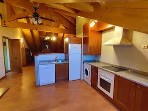 A compact kitchen with wooden beams, a built-in washing machine, a dishwasher, and a stove.