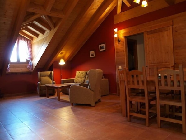 A cozy loft-style room with a high ceiling, wooden beams, a sofa, chairs, and a small table.