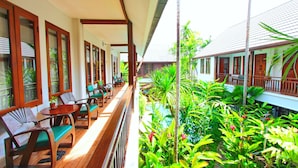 Un área de estar al aire libre con techo, muebles de madera y plantas tropicales.