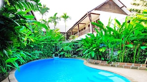 Una piscina rodeada de exuberante vegetación tropical, con un edificio que tiene un balcón al fondo.