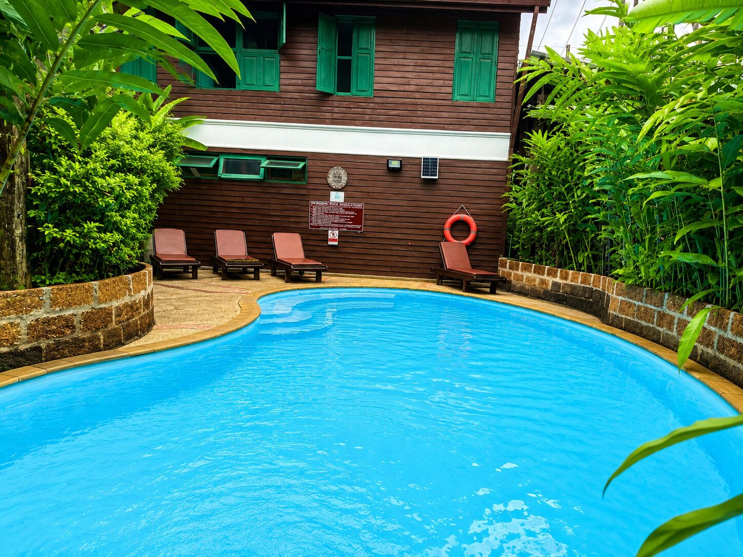A swimming pool with lounge chairs and a wooden building with green shutters.