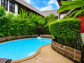 Une piscine entourée d’une végétation luxuriante et un bâtiment doté d’un toit en tuiles.