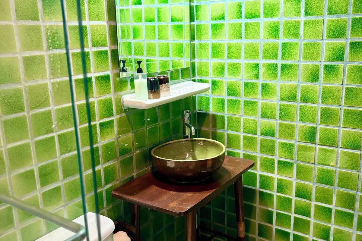 Een badkamer met groene mozaïektegels, een houten wastafel en een wit toilet.