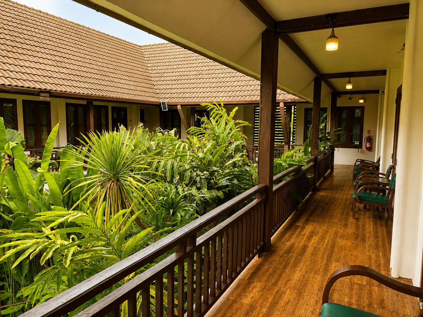 A covered outdoor area with a wooden deck, potted plants, and a row of chairs.
