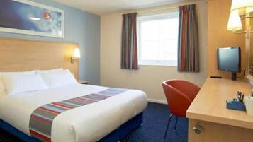 A hotel room with a bed, a desk with a chair, a television, and a window with curtains.