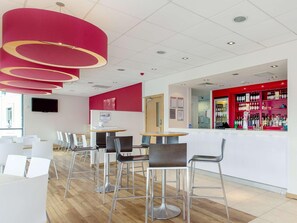 A modern bar area with a red and white color scheme, featuring a bar counter, seating area with chairs and tables, and a television mounted on the wall. - Travelodge Torquay (Torquay)