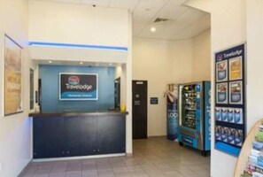 A Travelodge reception desk with a blue and white color scheme, a vending machine, and a poster on the wall. - Travelodge Chichester Central (Chichester)