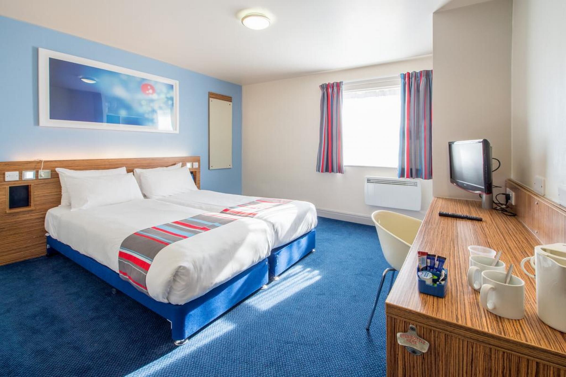 Une chambre d’hôtel avec un lit, un bureau avec une télévision, une chaise et une fenêtre avec des rideaux.