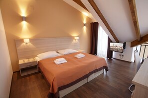 Un dormitorio con cabecera de madera, cama con colcha naranja, dos mesitas de noche y un televisor de pantalla plana montado en la pared.