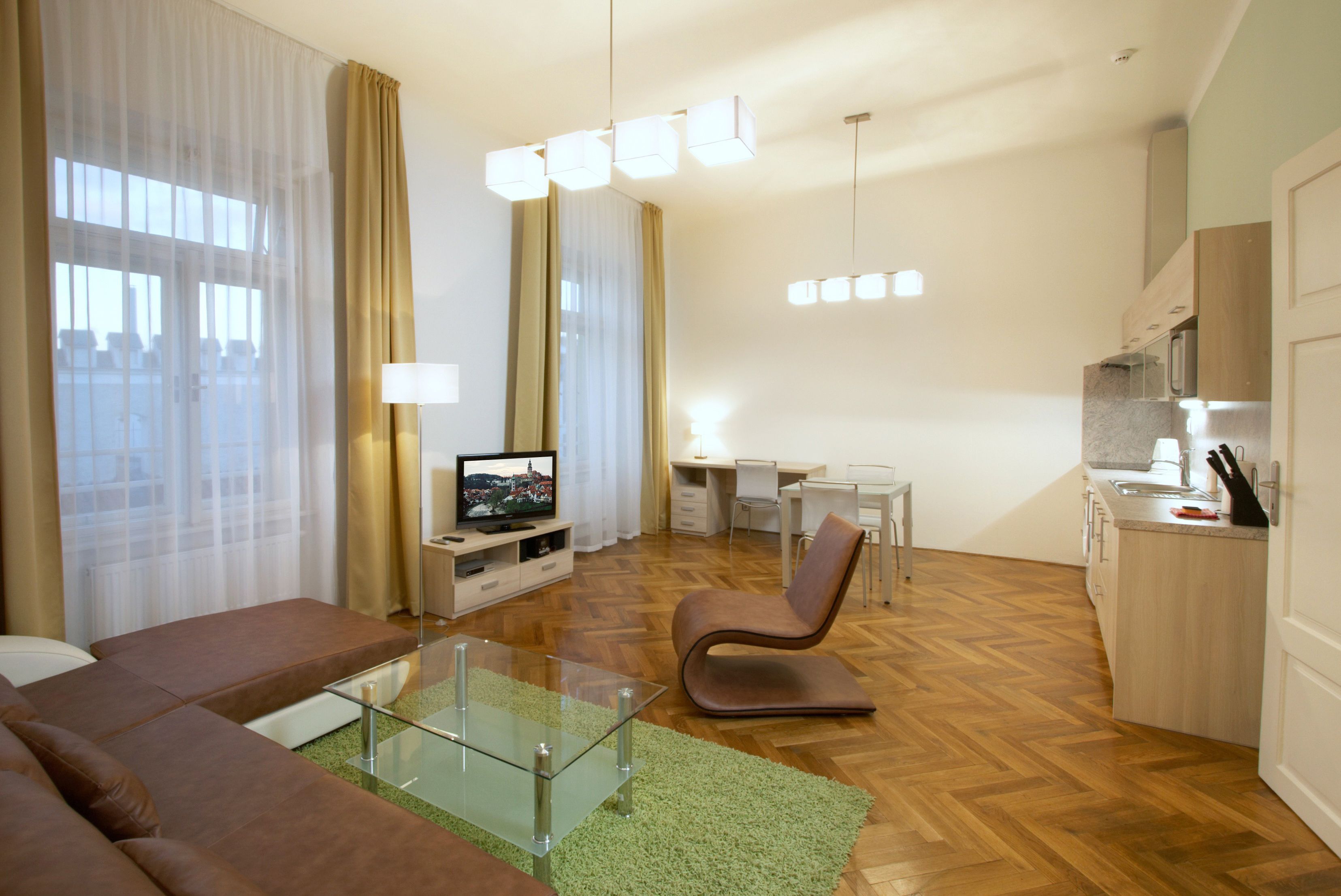 A modern living room with a glass coffee table, a brown sofa, a TV, and a dining area with a white table and chairs.