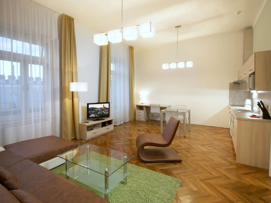 A modern living room with a glass coffee table, a brown sofa, a TV, and a dining area with a white table and chairs.