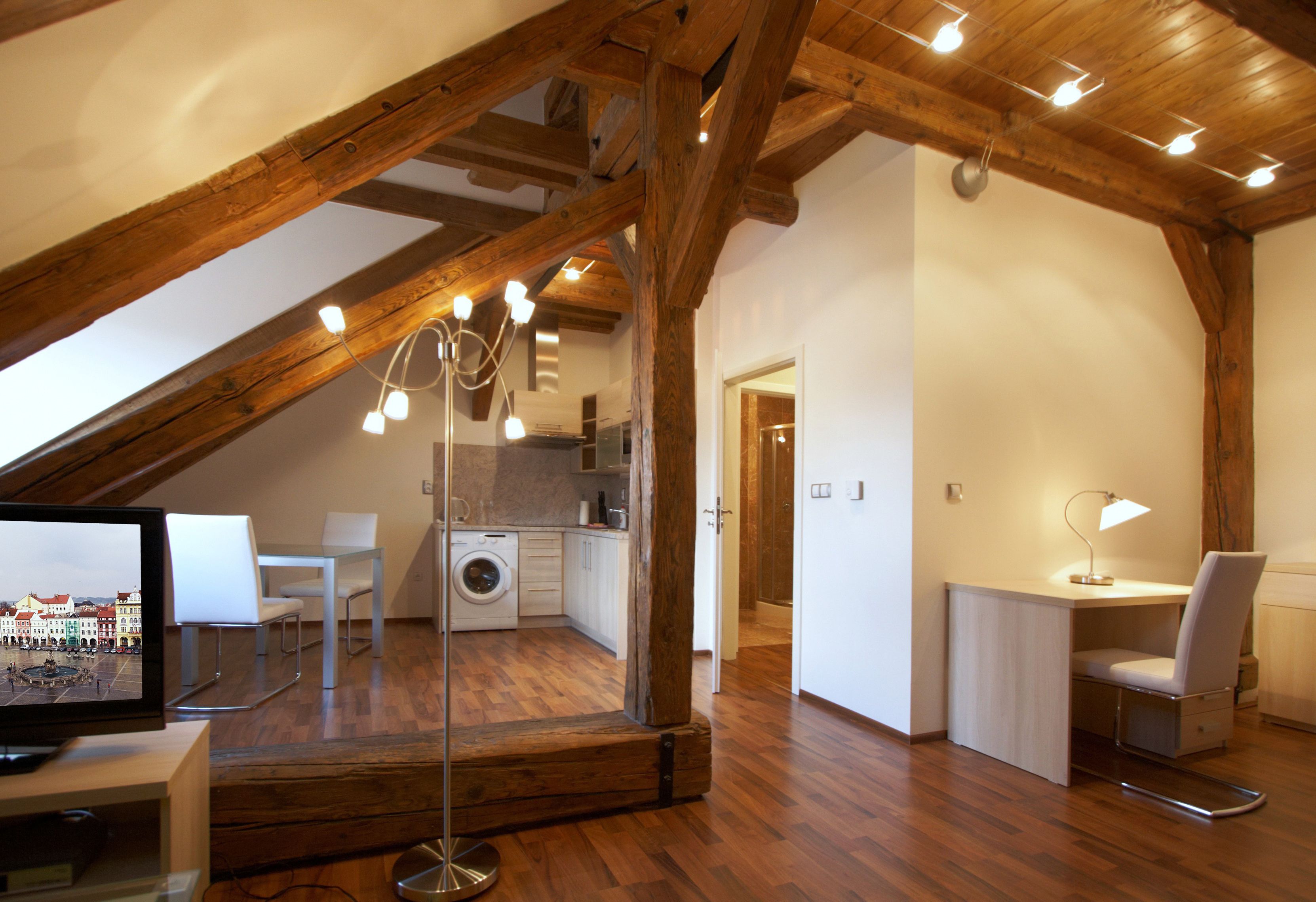 A spacious loft with a high ceiling, exposed wooden beams, a kitchen area, and a seating area with a TV.