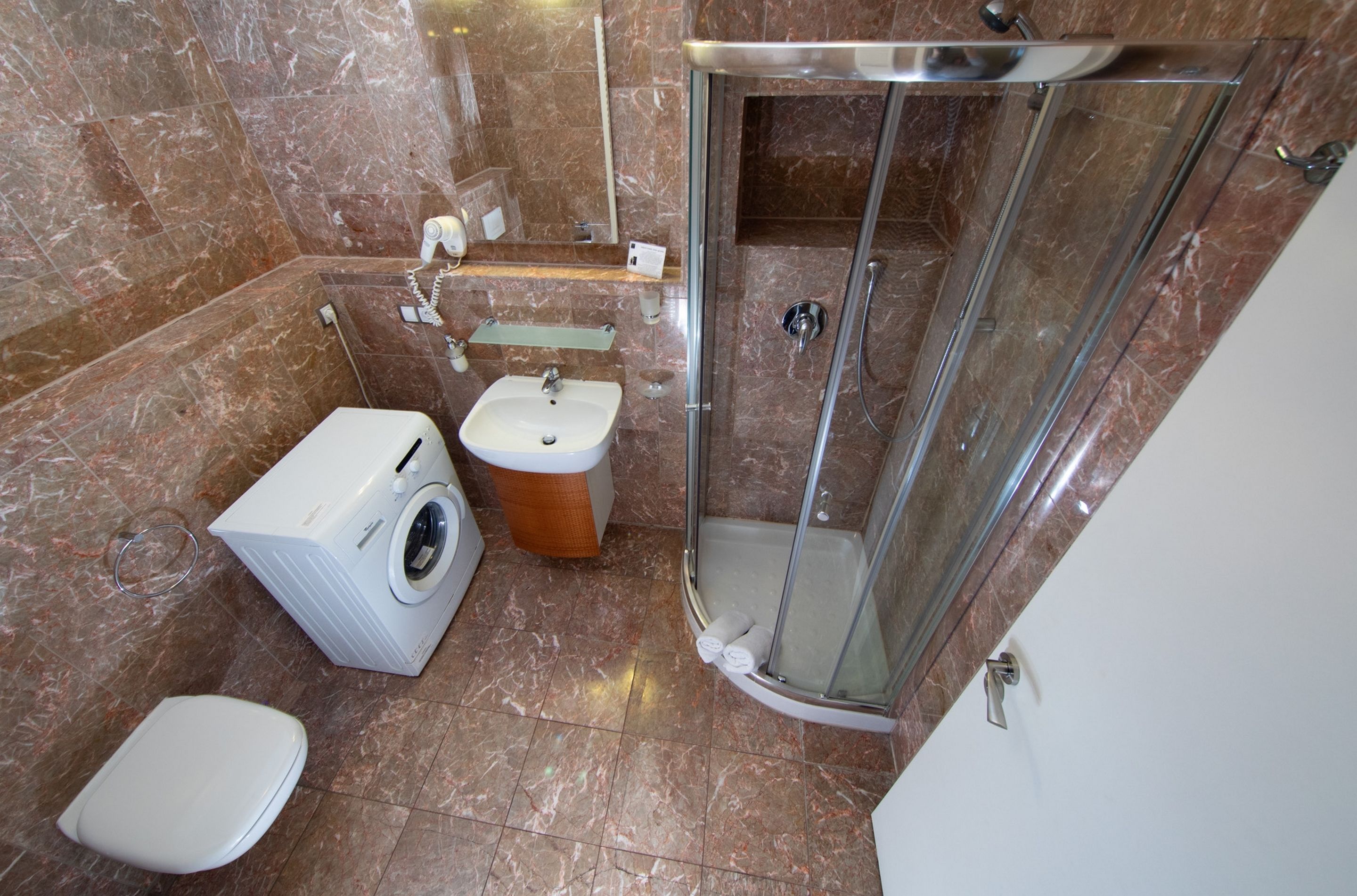 A compact bathroom with a washing machine, toilet, sink, and glass-enclosed shower.