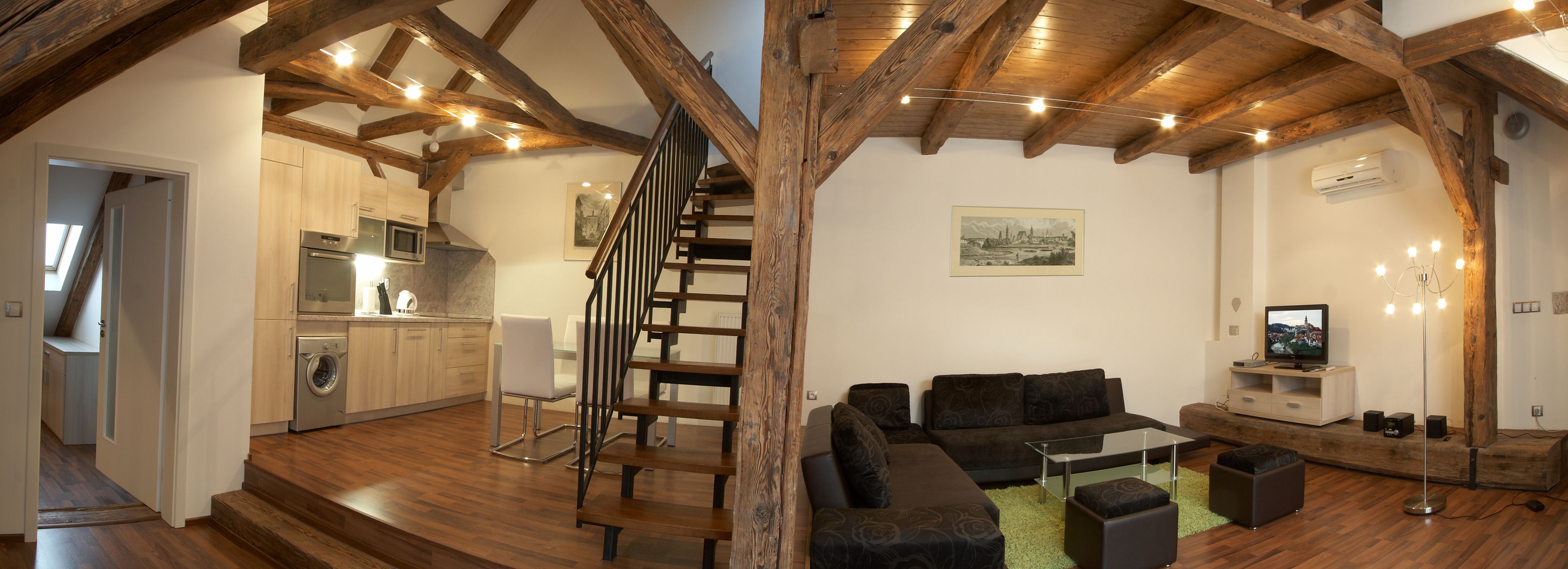 A modern interior with a wooden staircase, a kitchen with appliances, a living area with sofas and a TV, and a wooden ceiling.