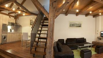 A modern interior with a wooden staircase, a kitchen with appliances, a living area with sofas and a TV, and a wooden ceiling.