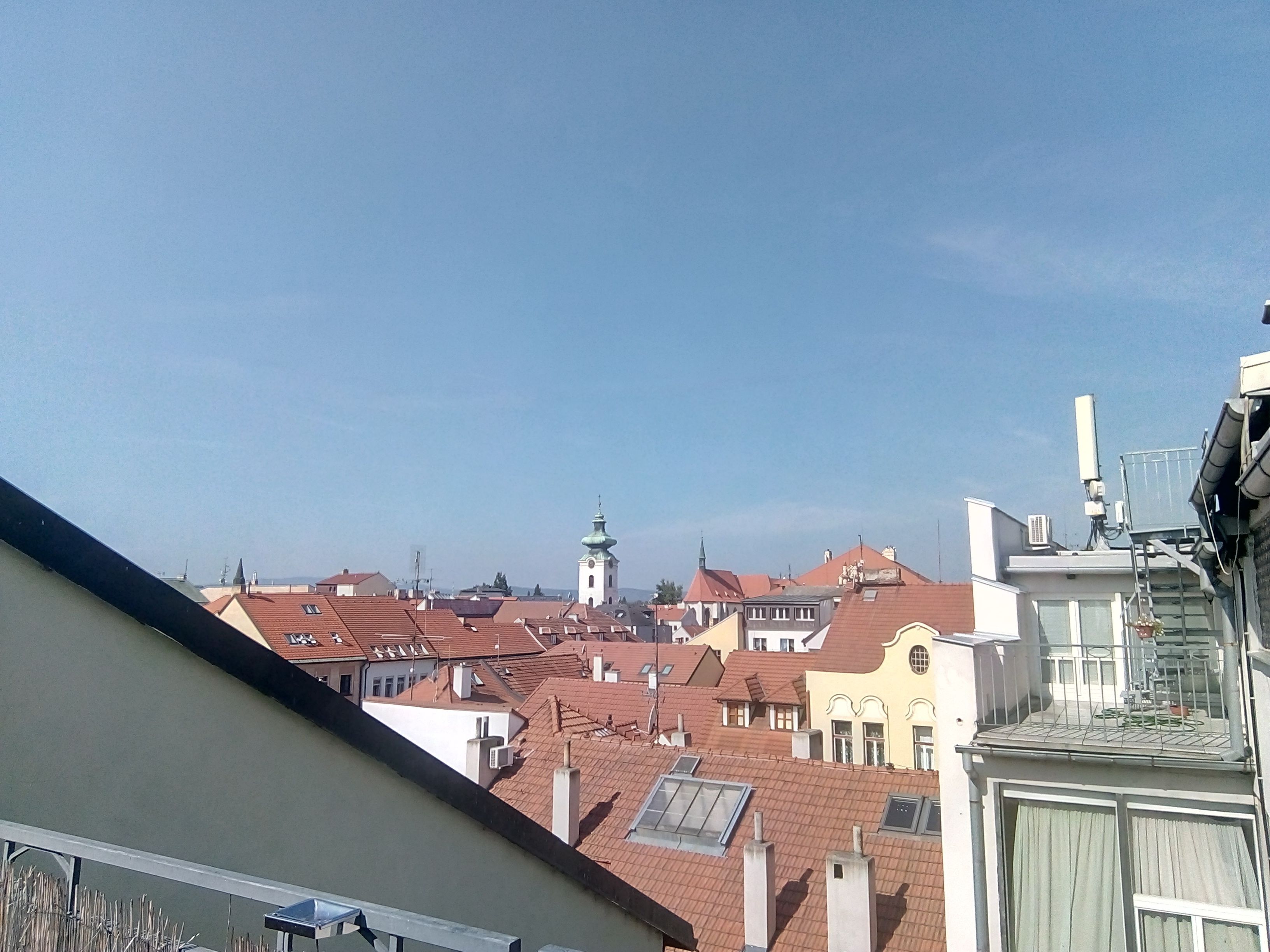 A cityscape with red-tiled roofs and a prominent church tower.