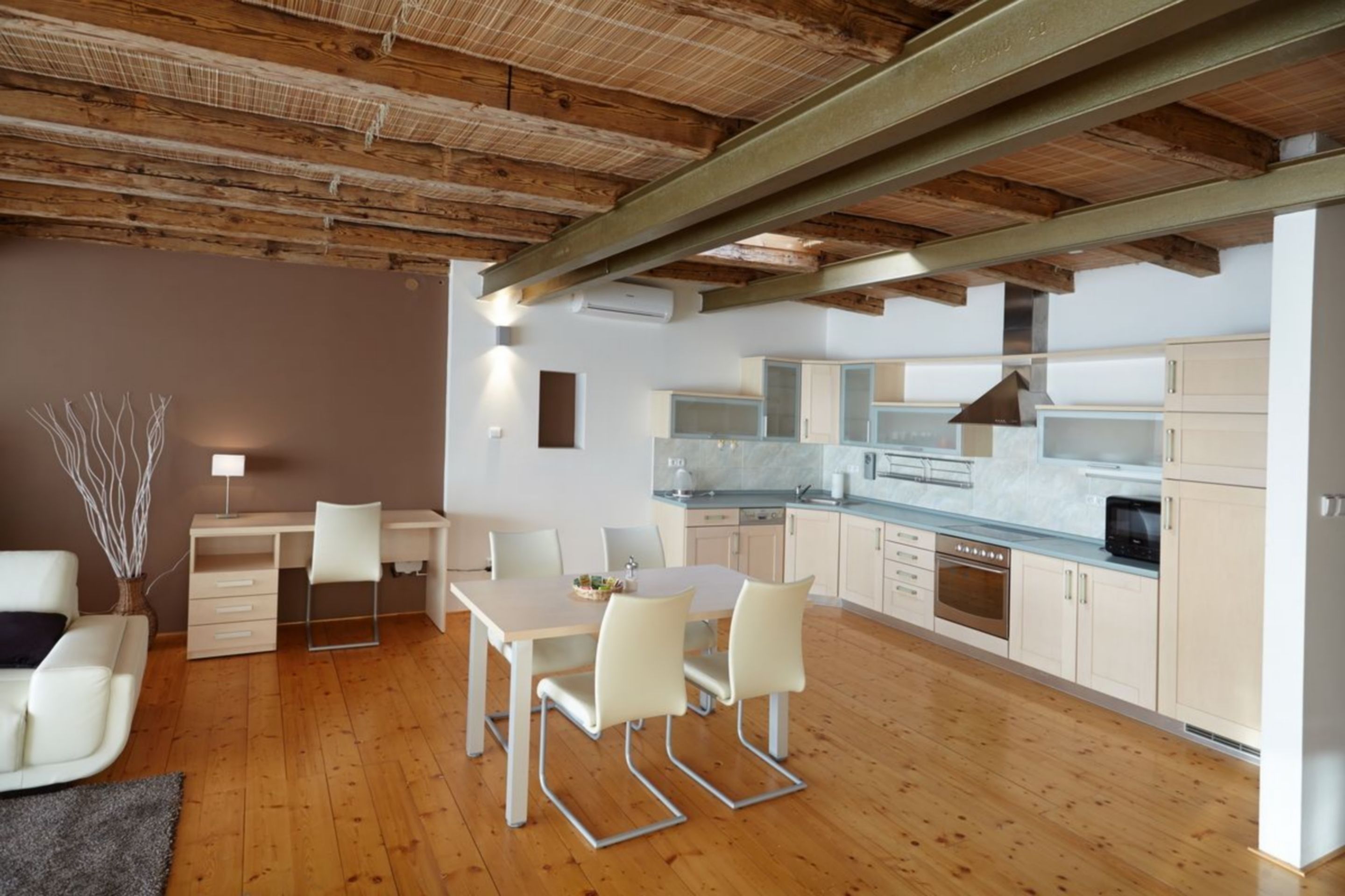 A modern kitchen with wooden beams, white cabinets, and a dining area with a table and chairs.