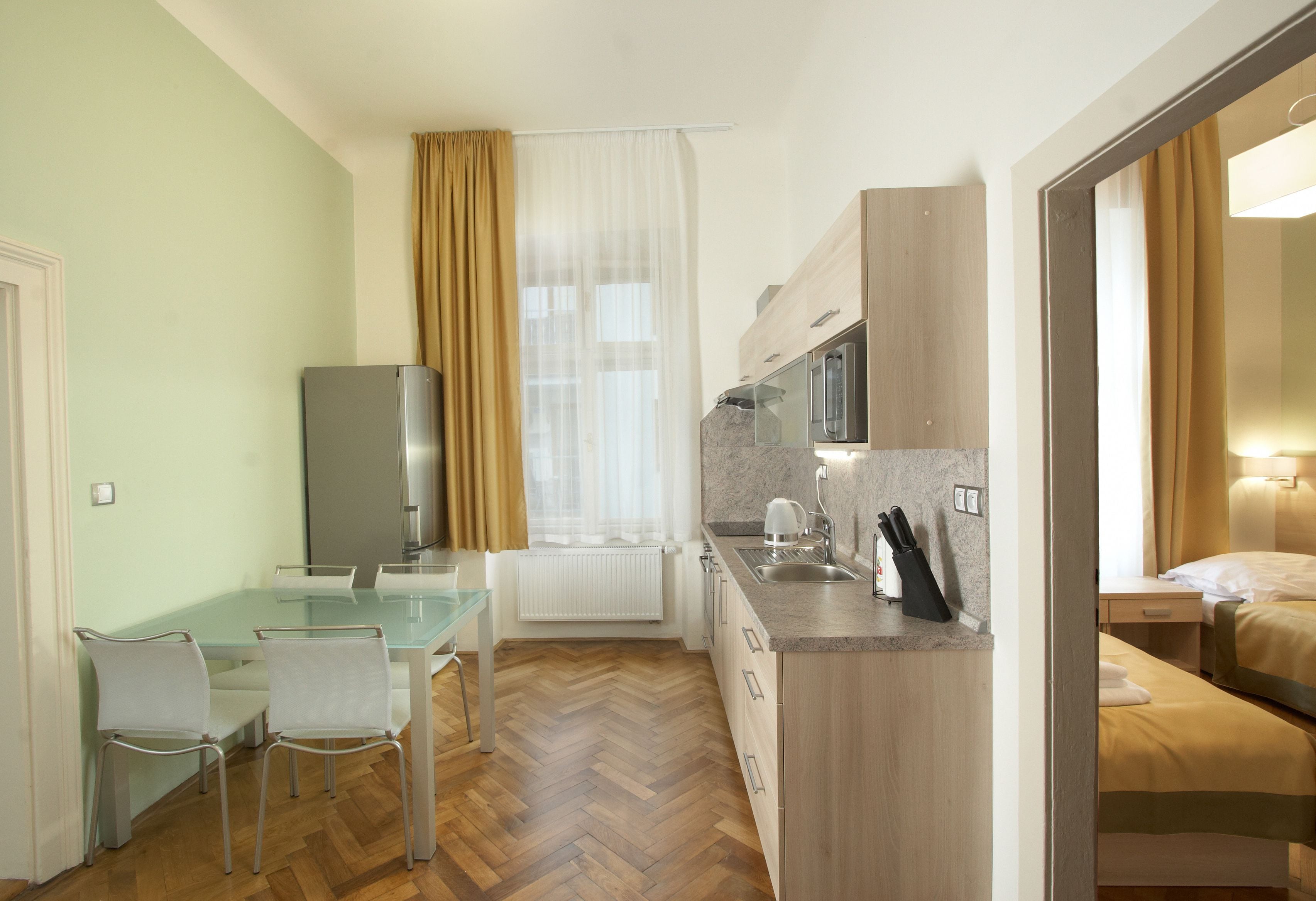 A modern kitchen with a glass dining table, white chairs, and a built-in oven.