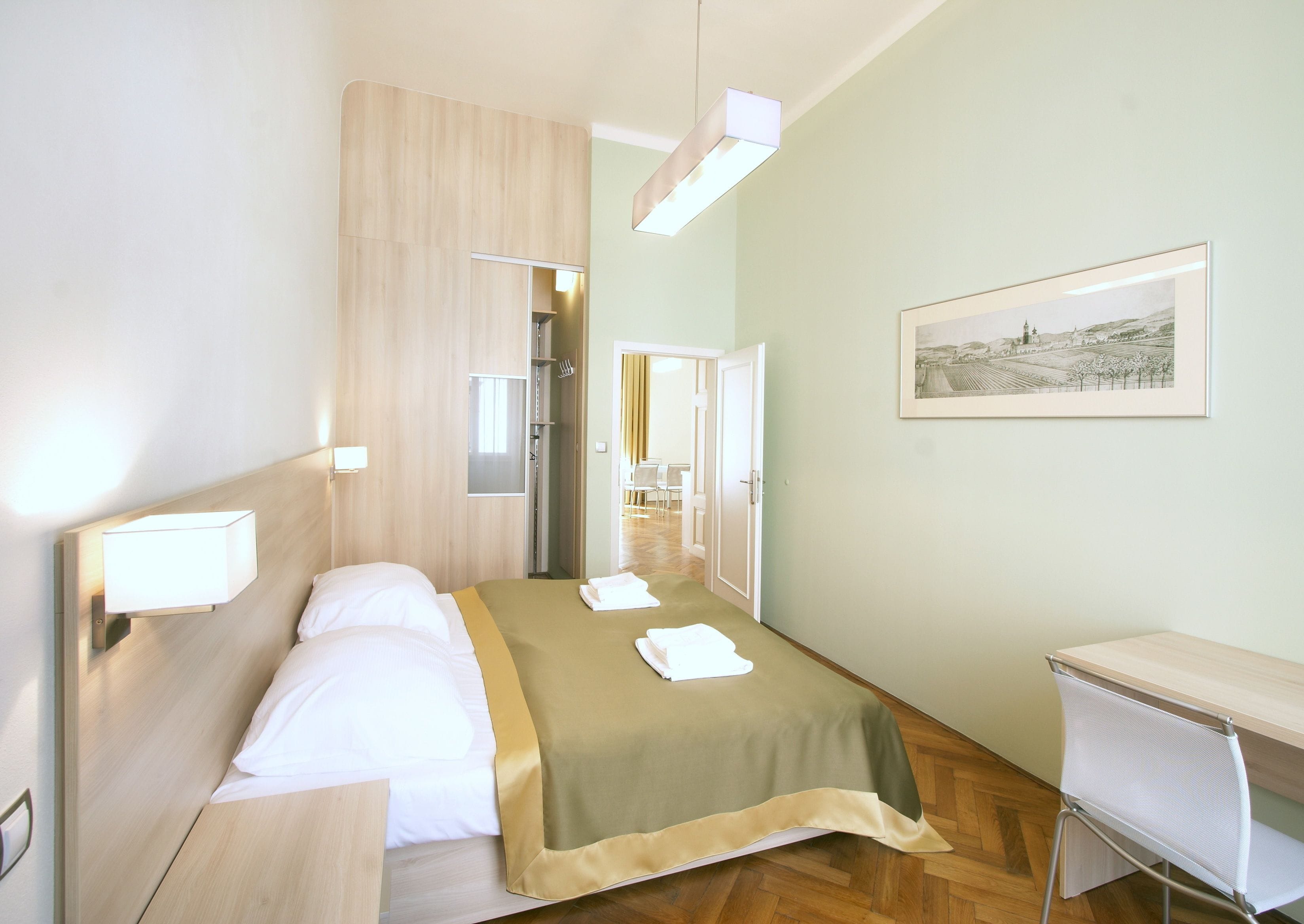 A hotel room with a bed, bedside table, desk, and a framed picture on the wall.