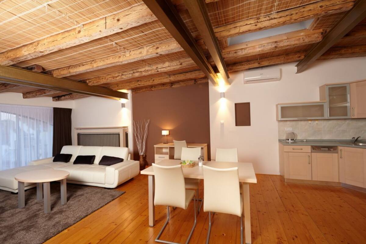 Una sala de estar moderna con techo de madera, un sofá, una mesa de comedor con sillas y una zona de cocina con armarios y un microondas.
