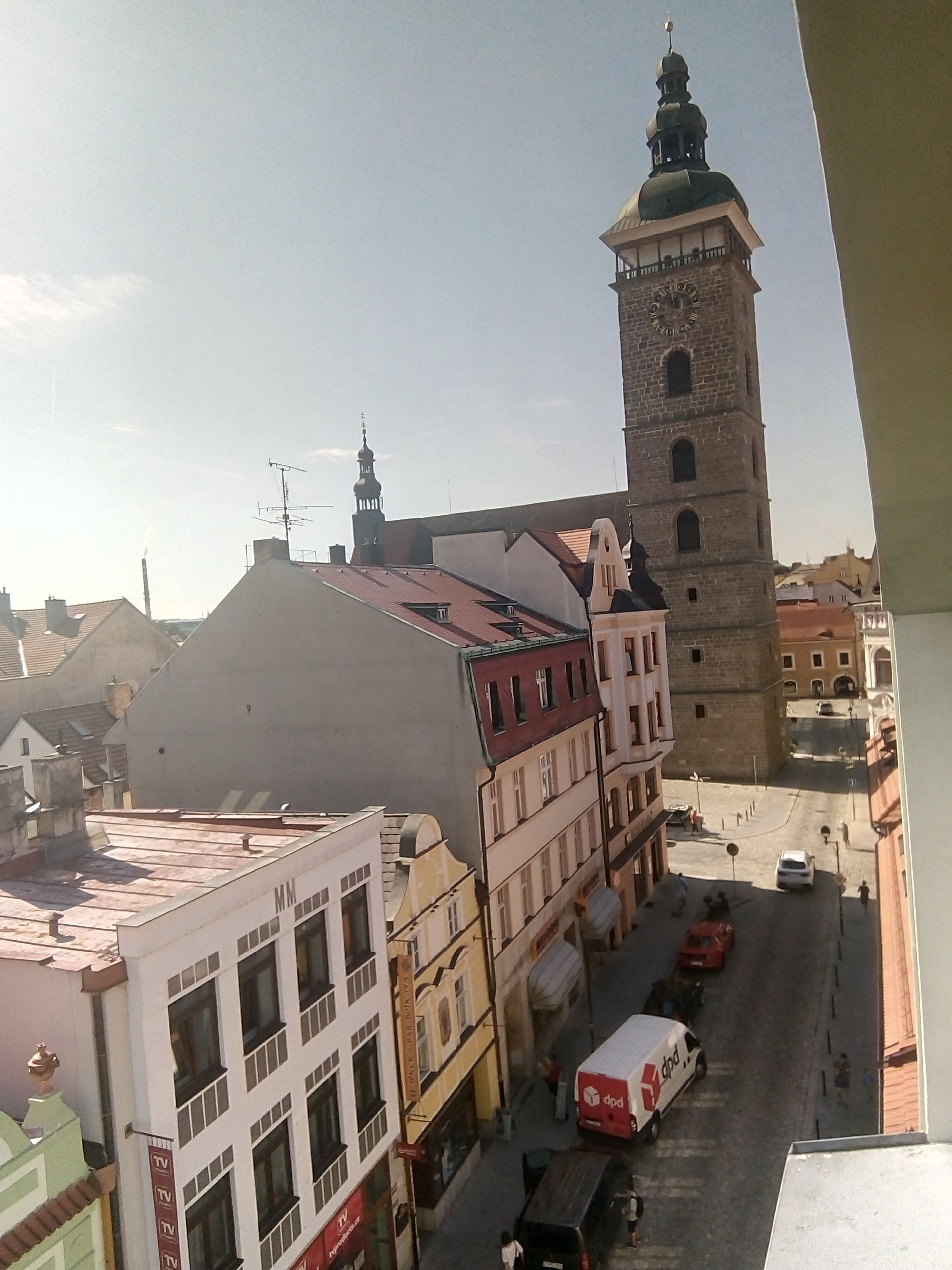 Blick auf eine Stadtstraße mit einem markanten Turm und einem Gebäude, an dem ein Schild mit dem Schriftzug 'TV' zu sehen ist.