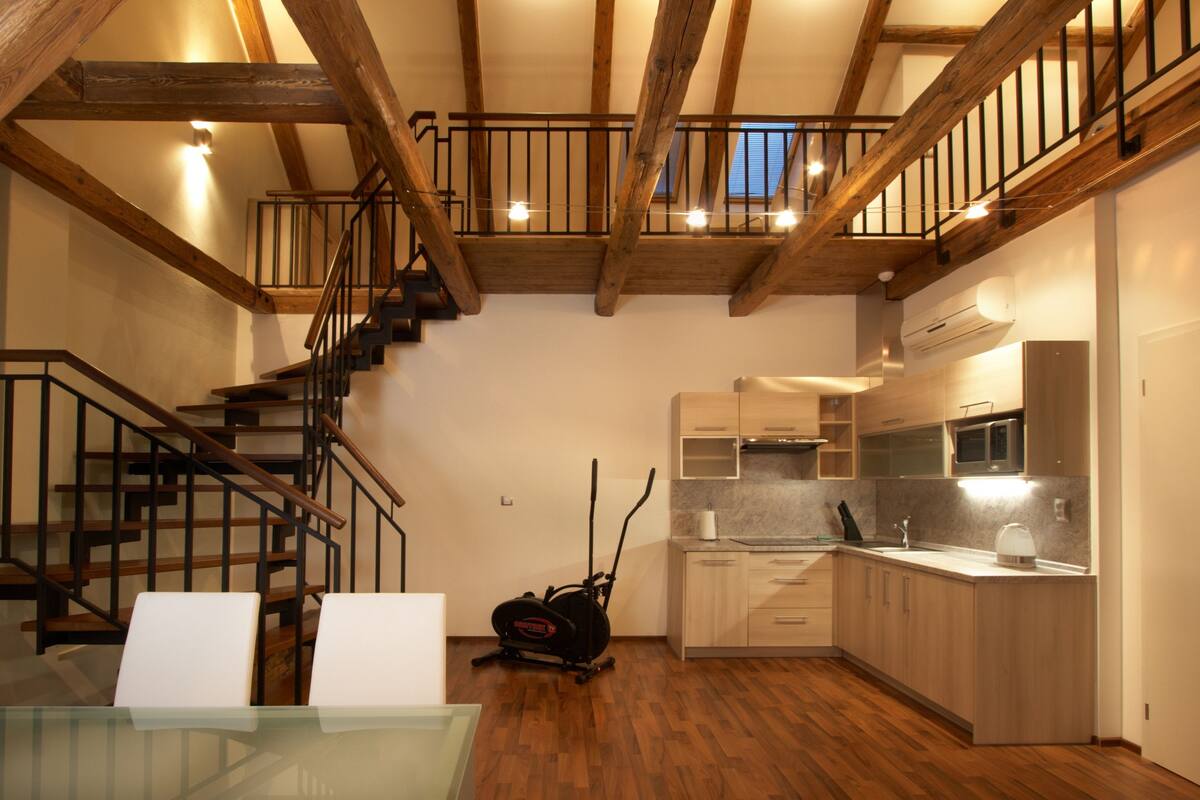 Una cocina amplia con vigas de madera, una mesa de vidrio y una escalera que conduce a un nivel superior.