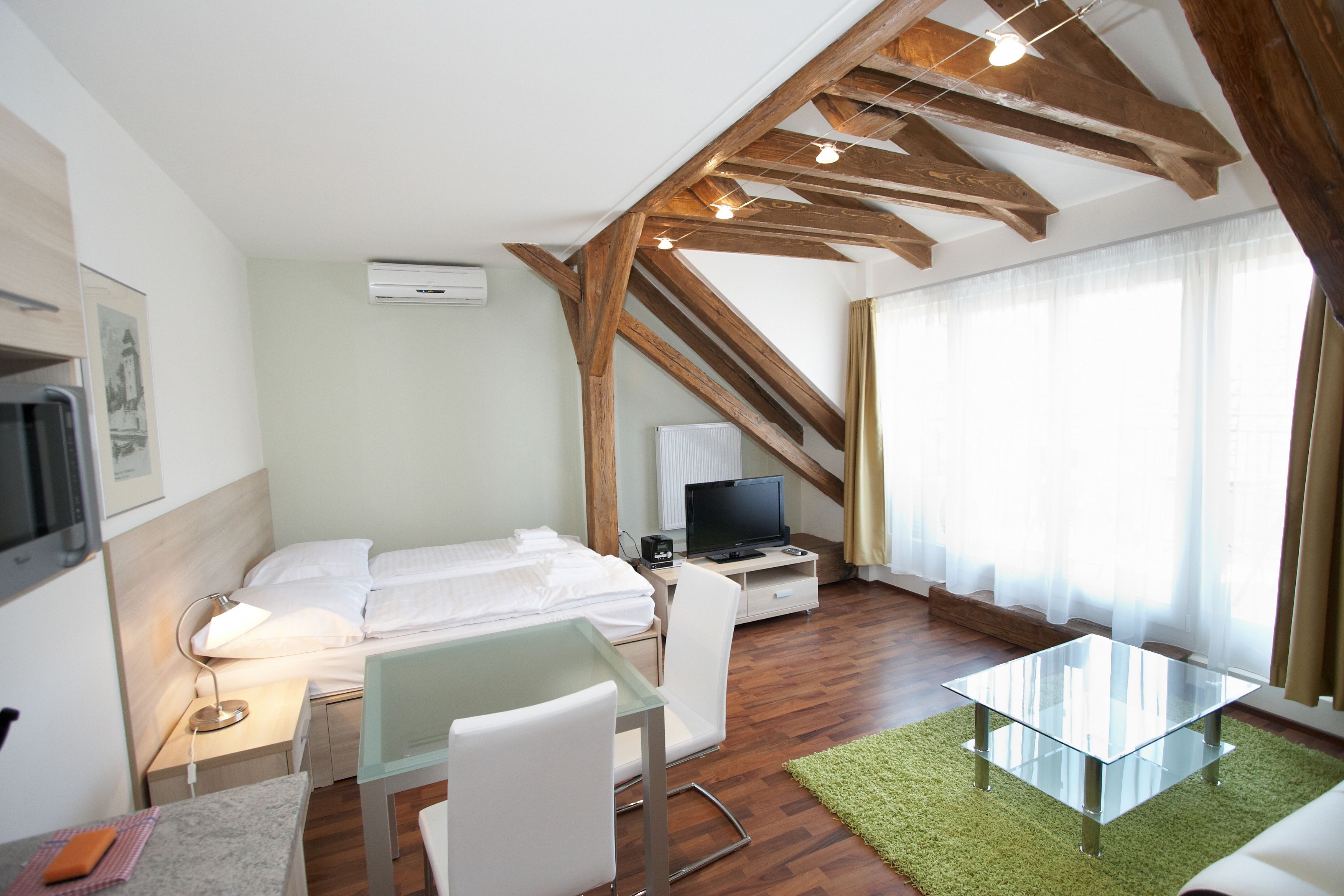 A bedroom with a bed, a desk, a chair, a TV, and a window with curtains.