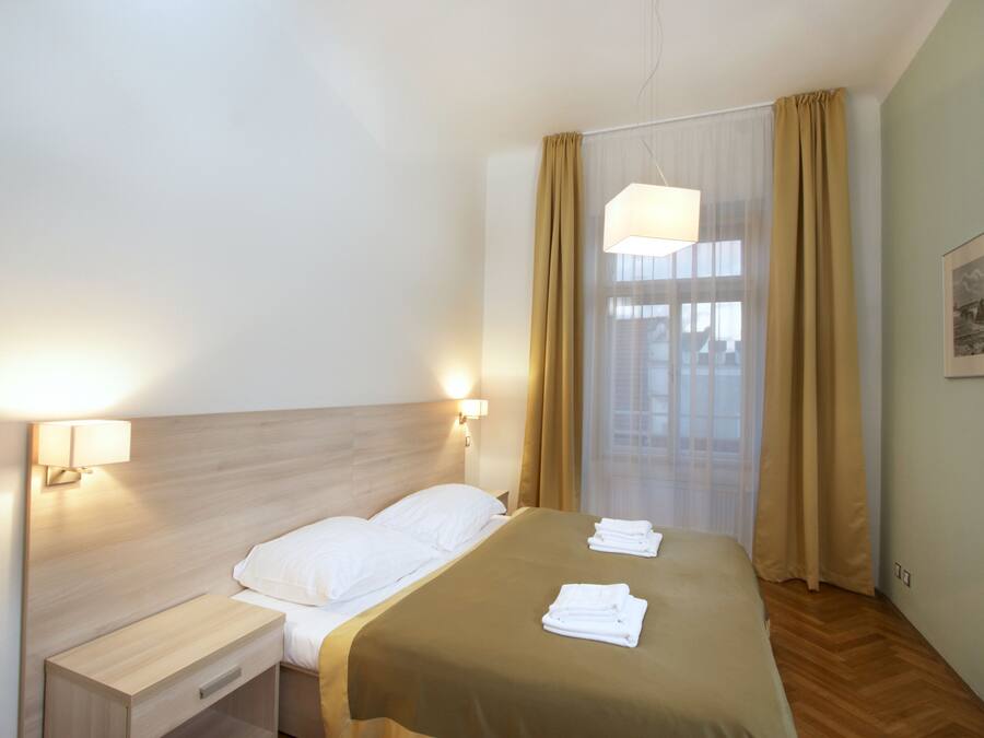 A hotel room with a bed, a nightstand, a lamp, and a window with curtains.