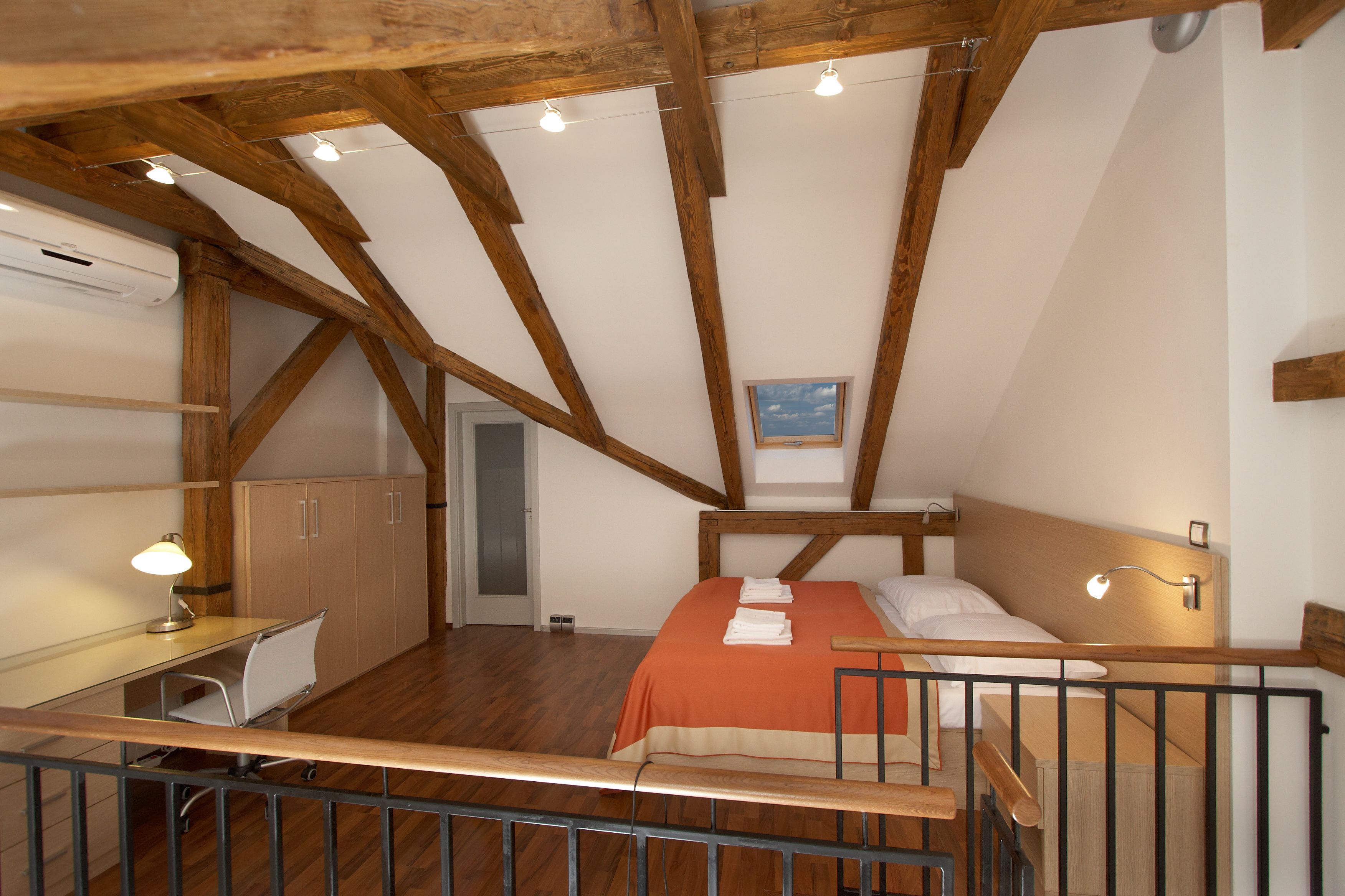 Un dormitorio con techo de madera, una cama, un escritorio y una silla.
