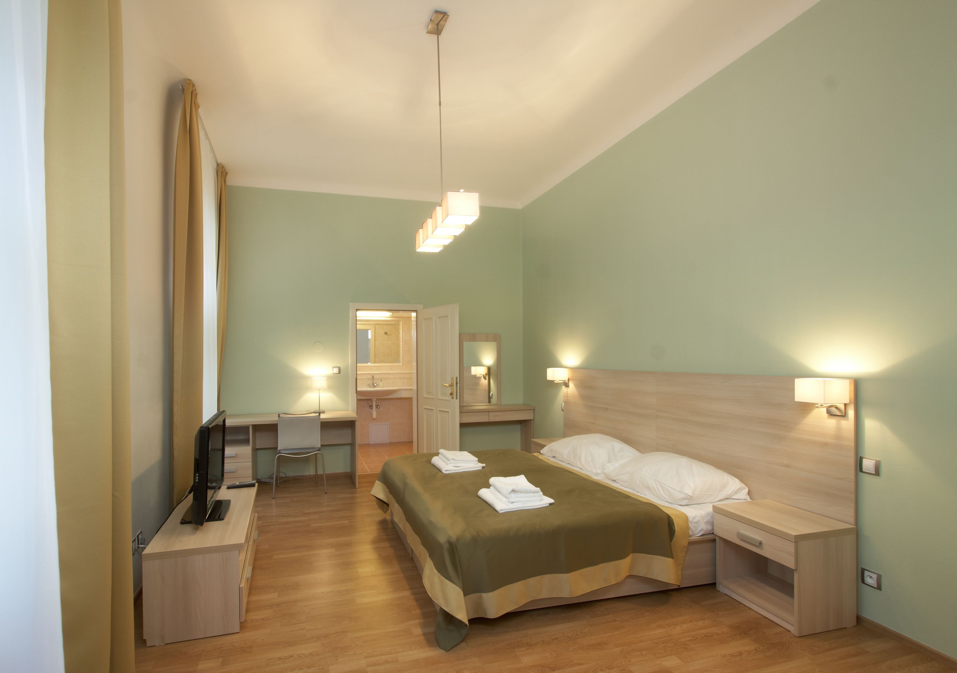 A bedroom with a bed, bedside tables, a desk, a chair, and a television.