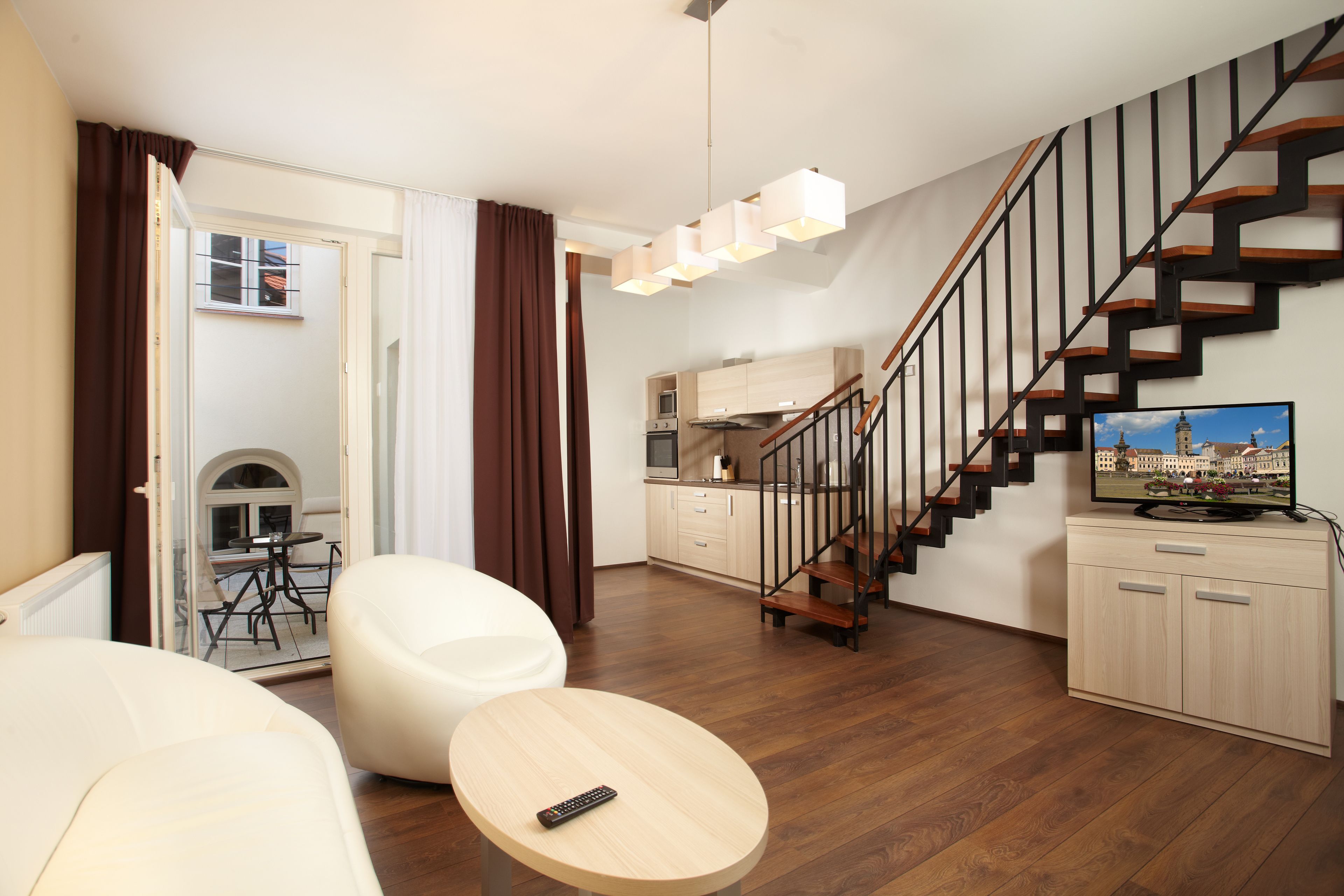 A modern living room with a sofa, a round coffee table, a TV on a stand, a staircase, and a kitchen in the background.