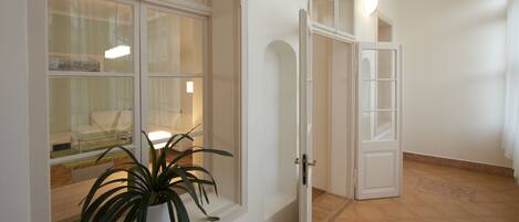 A room with a large window, a radiator, a potted plant, and a door leading to another room.