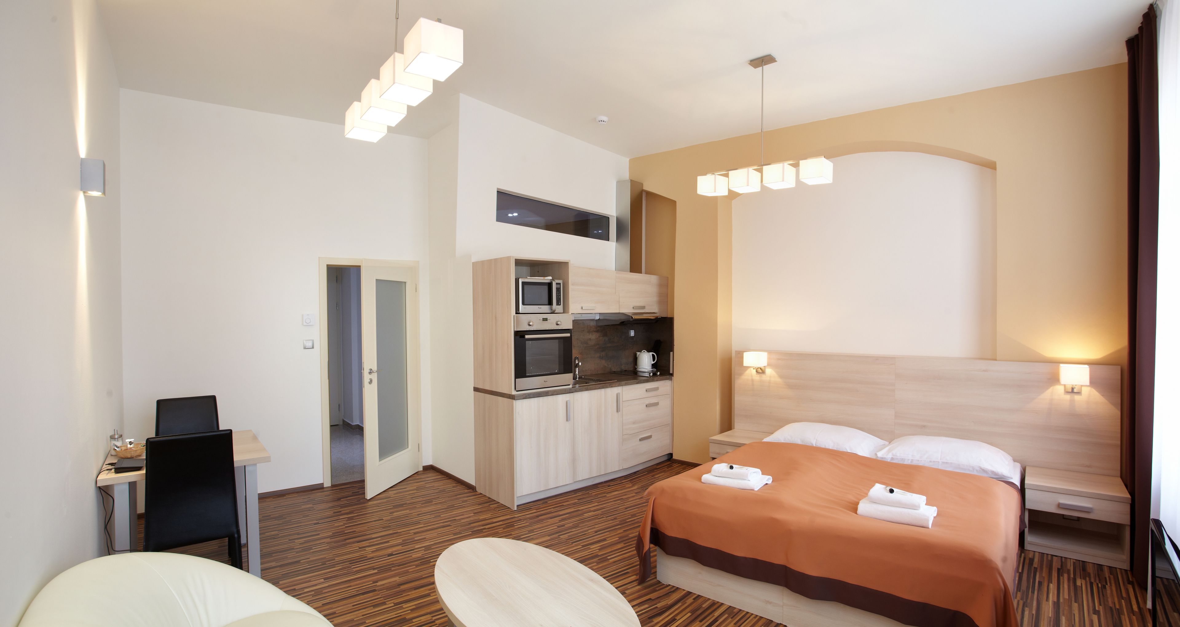 A hotel room with a bed, bedside tables, a desk, a microwave, and a kitchenette.