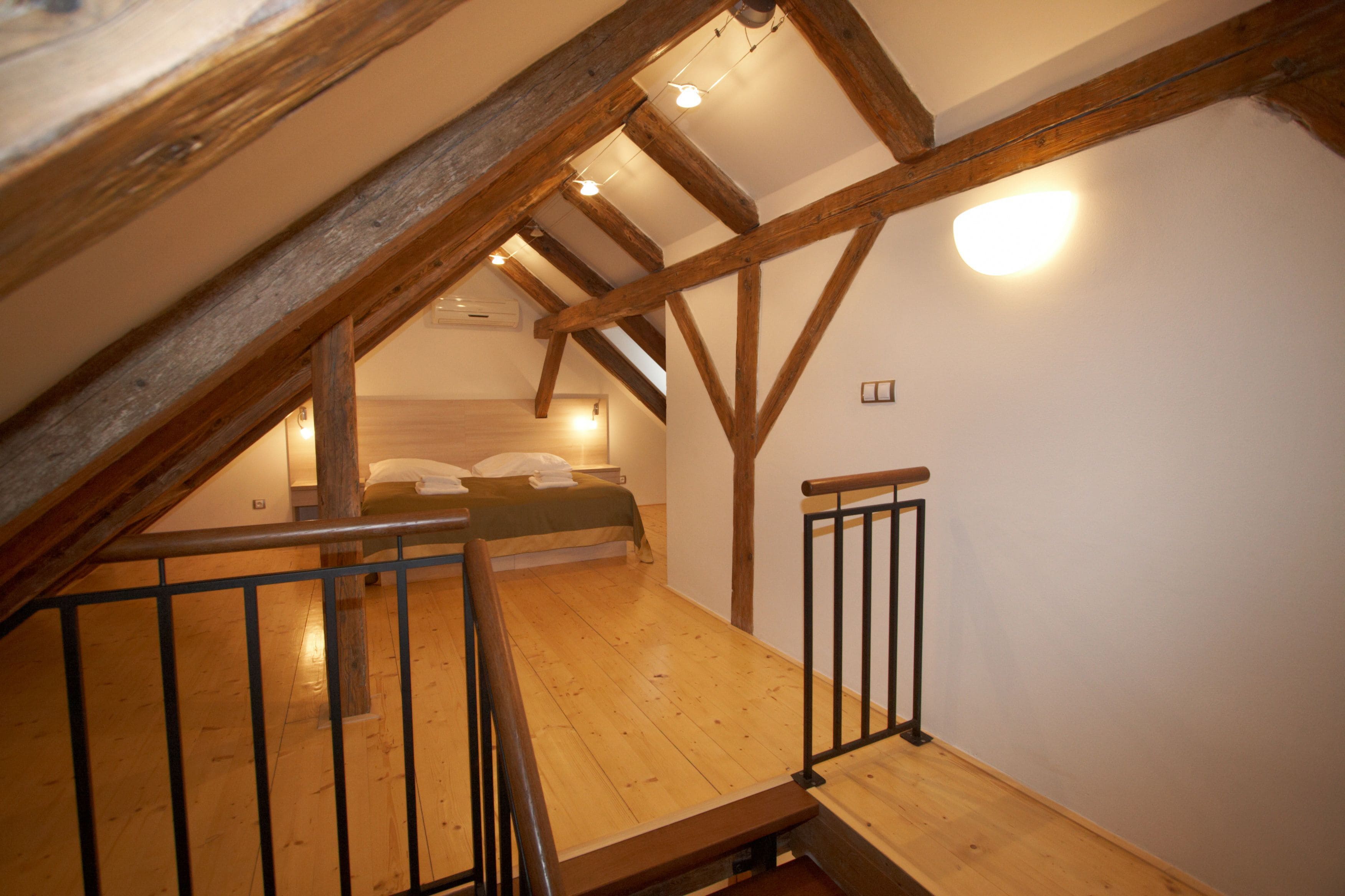 A wooden loft bedroom with a sloped ceiling, a bed, and a small seating area.